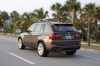 Driving 2013 BMW X5 xDrive50i in Sparkling Bronze Metallic from a rear left three-quarter view